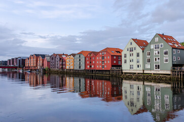 A row of typical colourful Norwegian houses built on pillars on top of a water surface. Reflecting on the water surface.