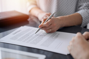Business people signing contract papers while sitting at the glass table in office, closeup. Partners or lawyers working together at meeting. Teamwork, partnership, success concept.