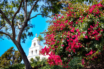 Bright Pink Bougainvillea Flowers Bloom and Contrast against a Bright Blue Sky at the White Façade of the Mission Basilica San Diego de Alcala in San Diego, California, USA