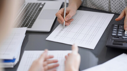 Woman accountant counting and discussing taxes with a client or a colleague while using a calculator and laptop computer. Business audit team.