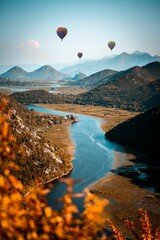 Vertical shot of air-balloons flying above a river between mountains