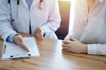 Doctor and patient  discussing something while sitting near each other at the wooden desk in clinic, view from above. Medicine concept.