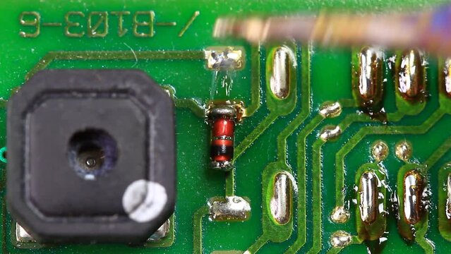 Engineer desolders and removes a surface mounted germanium diode. Technician desoldering using a soldering iron on the printed circuit board for remove part components. Static Macro Shot
