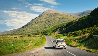 Fototapeta Beautiful landscape scenery with white car driving on empty scenic road trough nature and mountains at Delphi, county Mayo, Ireland  obraz