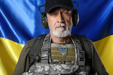 Mature soldier in headphones against flag of Ukraine, closeup