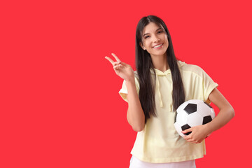 Young woman with soccer ball showing victory gesture on red background