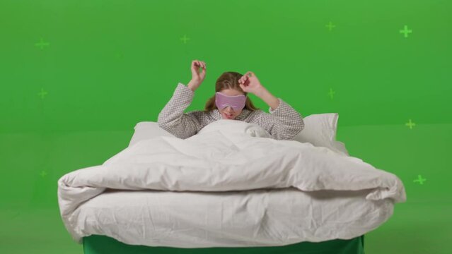 Happy sleepy young adult woman waking up lying in comfortable white bed. Positive pretty girl stretching enjoying early good morning. Strong wind blowing in face on green screen chroma key background