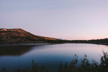 Scenic shot of a still lake surrounded by a hillside and plants at a calm sunset