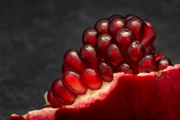 Macro shot of a piece of a pomegranate with stacked juicy seeds, on a black background