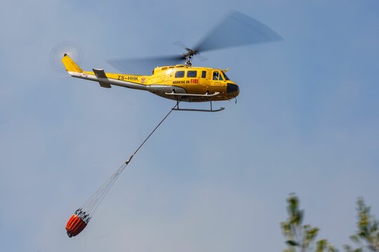 Low angle shot of a Huey helicopter carrying a container of water to extinguish the fire