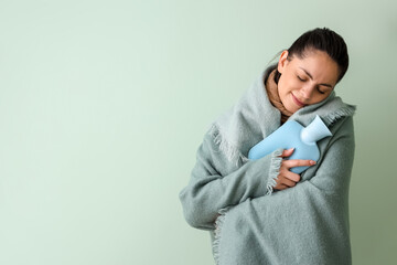 Ill young woman in plaid with hot water bottle on green background