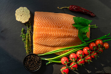 Top view of fresh raw salmon fish steak with spices on a dark stone background. Salt, spices, seasonings and other ingredients.