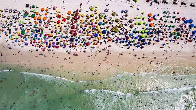 Drone view on the beach with sea and waves and white sand, tourists with umbrella