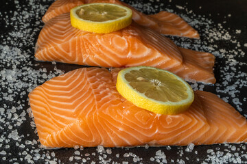 Top view of fresh raw salmon fish steak with spices on a dark stone background. Salt, spices, seasonings and other ingredients.