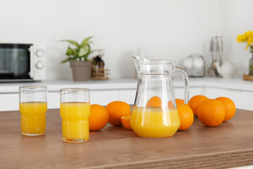 Jug with glasses of juice and oranges on table in kitchen