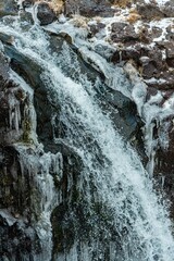 Scenic view of a waterfall on rocky mountain covered with snow on a sunny day. Vertical shot