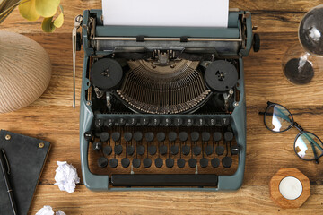 Vintage typewriter with eyeglasses, hourglass and notebook on brown wooden background
