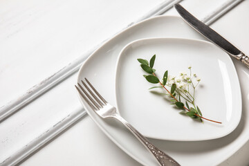Plates with silver cutlery and flowers on white wooden background