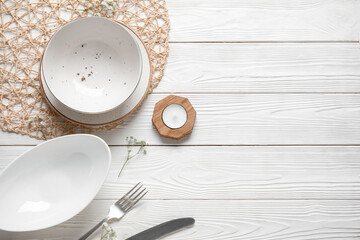 Wicker mat with plates, cutlery and candle on white wooden background