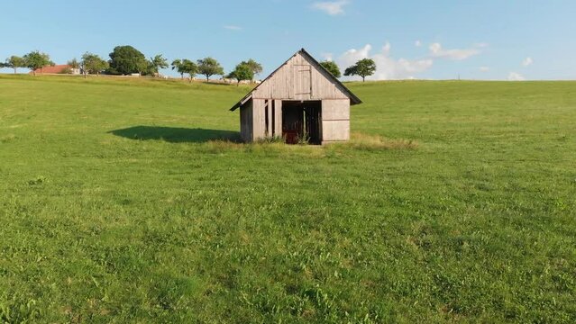 Flug mit Drohne &uuml;ber eine Wiese auf einem Bauernhof auf eine gruselige Holzh&uuml;tte Scheune mit dunklem Eingang zu und anschlie&szlig;endem Steigflug zu einer Kuh Herde zwischen B&auml;umen in 4k