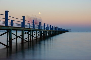Fototapeta na wymiar Calm sea and wooden dock against the pink sunset sky with a full moon