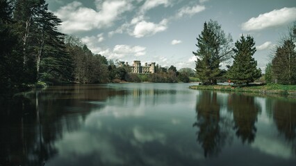 Beautiful Castle of Eastnor surrounded by trees and a lake against the blue sky