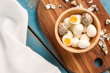 Board with bowl of boiled quail eggs and shells on blue wooden background