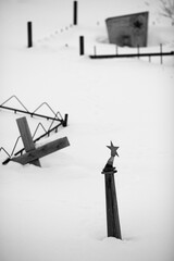 Graves covered with snow in an old cemetery in the Far North of Russia in the Arctic. Soviet star and cross in the snow. Memories and sad mood. Black and white photography.