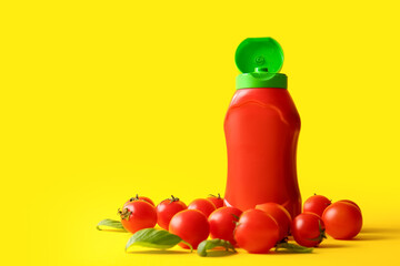 Bottle of ketchup and tomatoes on yellow background
