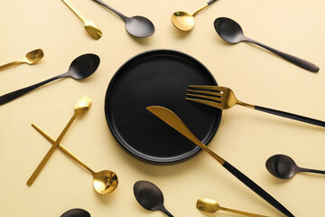 Golden fork with knife, spoons and plate on yellow background