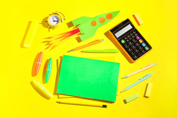 Paper rocket with calculator, alarm clock and different stationery on yellow background