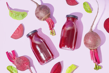 Bottles of healthy beet juice and spinach on lilac background