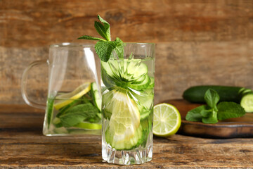 Glass and jug of infused water with cucumber slices on wooden background