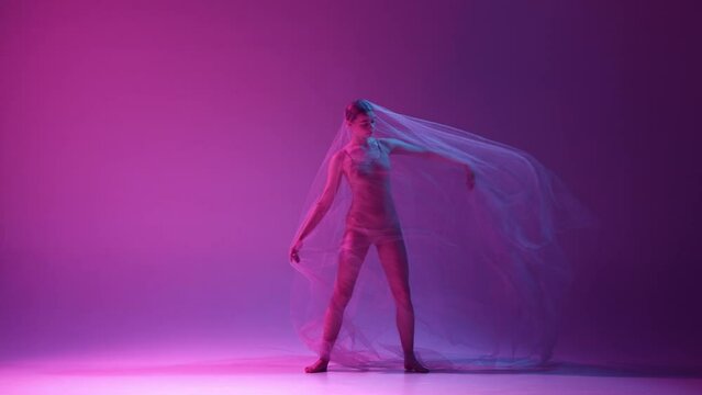Tender, talented young girl, ballerina in beige bodysuit dancing with transparent veil over gradient pink purple studio background in neon light. Concept of classical art, dance, beauty, inspiration