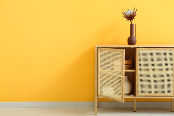 Wooden chest of drawers with protea flower and decor near orange wall in room