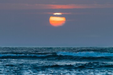 Scenic shot of the setting sun under the clouds and the waves of the turbulent sea