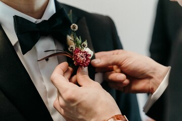 Closeup shot of a man helping the groom to wear a decor