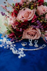 Vertical closeup shot of wedding jewelry and a rose bouquet on a blue table