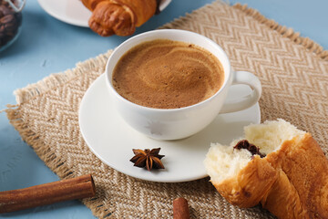 Cup of delicious espresso and croissant on blue background, closeup