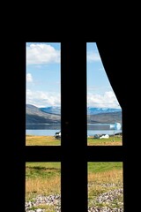 Fototapeta premium Vertical shot from the inside of a window overlooking a grass field on the coast of a lake