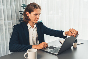 Businessman in black suit working on laptop at his workspace desk. Smart executive researching financial data and planning marketing strategy on corporate laptop at modern workplace. Entity