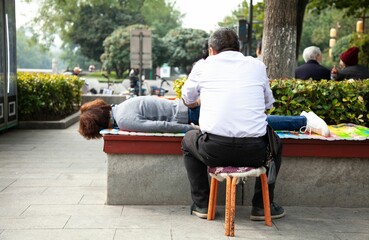 Fototapeta premium Male sitting on a chair while giving a massage to a female lying on a park bench