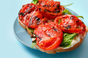 Plate of sandwiches with tasty grilled tomatoes and arugula on blue background