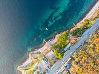 Aerial bird's eye view of the coast of an ocean next to a street and houses on a sunny day