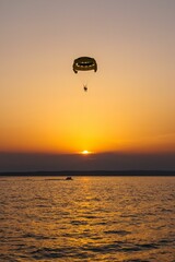 Vertical shot of two people paragliding and enjoying the beautiful sunset visible on the horizon