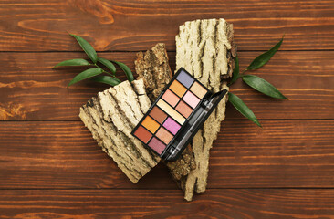 Palette of eyeshadows, tree bark and plant leaves on wooden background