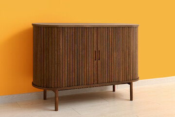 Stylish wooden chest of drawers near orange wall in room