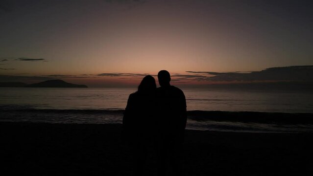 Silhouette of a male and a female couple at a beach against a sunset horizon