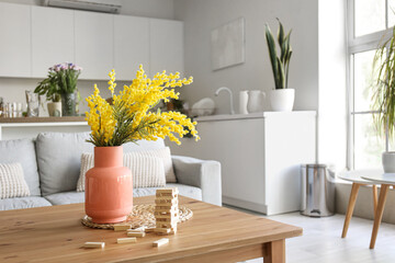 Vase with mimosa flowers and wooden blocks for game on table in open space studio apartment
