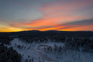 Beautiful view of a snowy forest with trees and hills during orange sunset